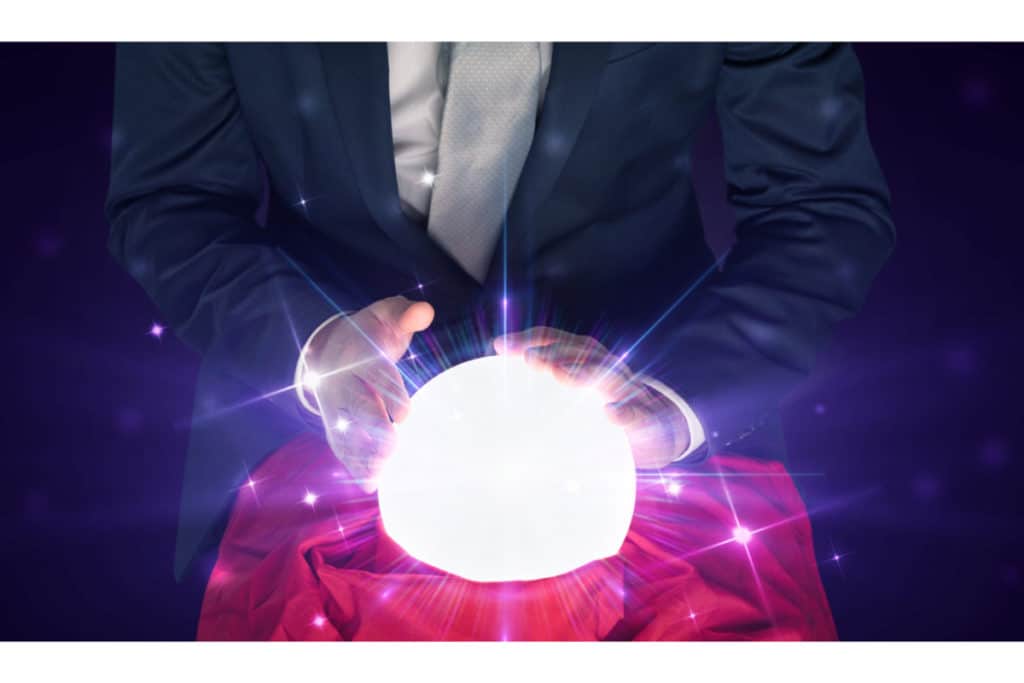 un homme en costume touche une boule de cristal lumineuse qui est entre ses mains, posée sur une table sur laquelle est posée un tissu rouge.