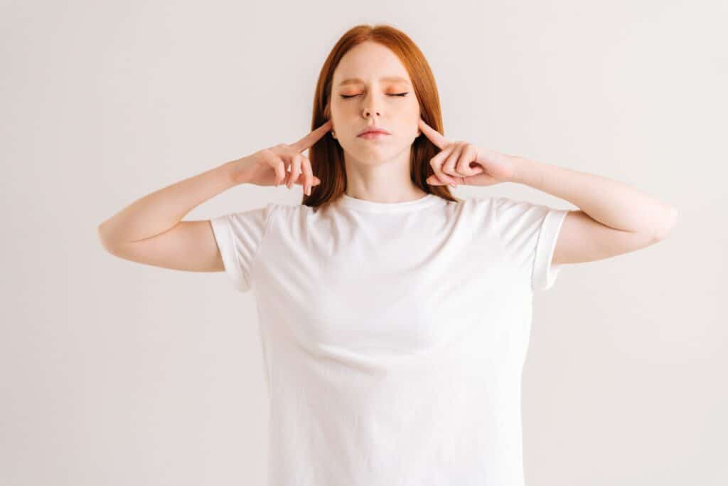 Une femme méditant en fermant les yeux et en bouchant ses deux oreilles avec ses doigts
