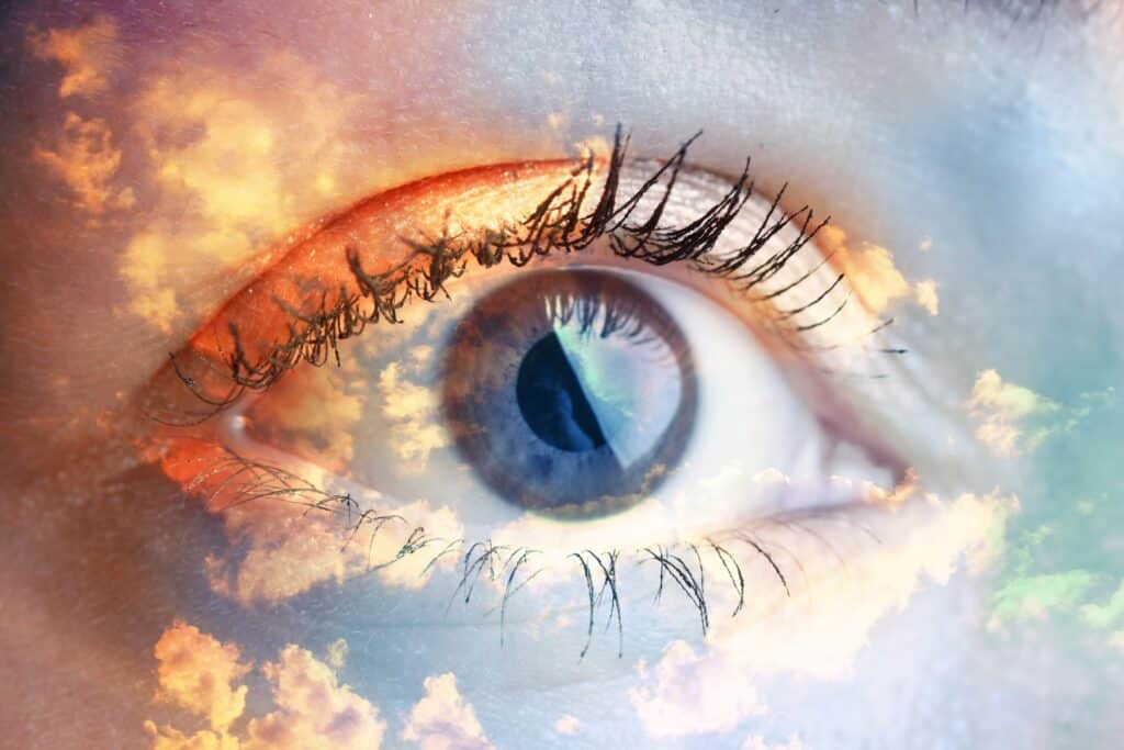 Une double exposition de la photo d'un œil humain avec un fond de nuage de différentes couleurs.