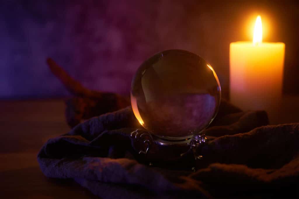 une boule de cristal posée près d'une bougie blanche sur une table de divination dans un atmosphère sombre