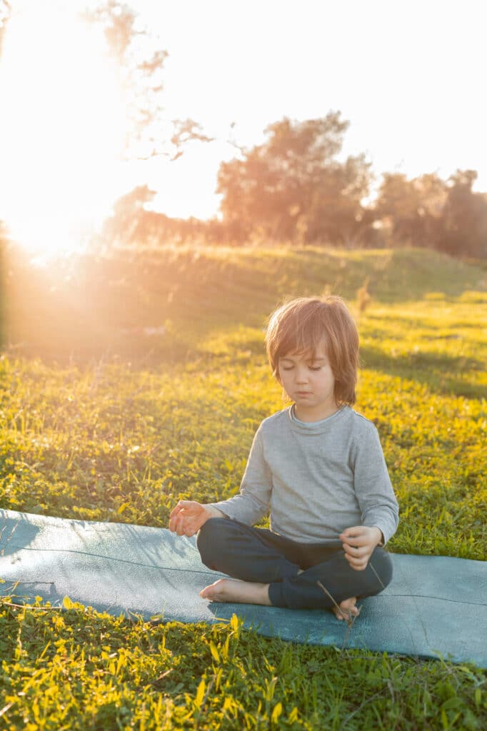 Un petit garçon méditant en pleine nature, assis sur un tapis.